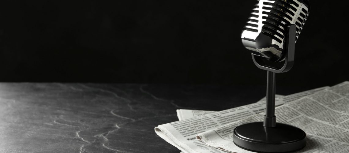 Newspapers and vintage microphone on dark stone table, space for text. Journalist's work